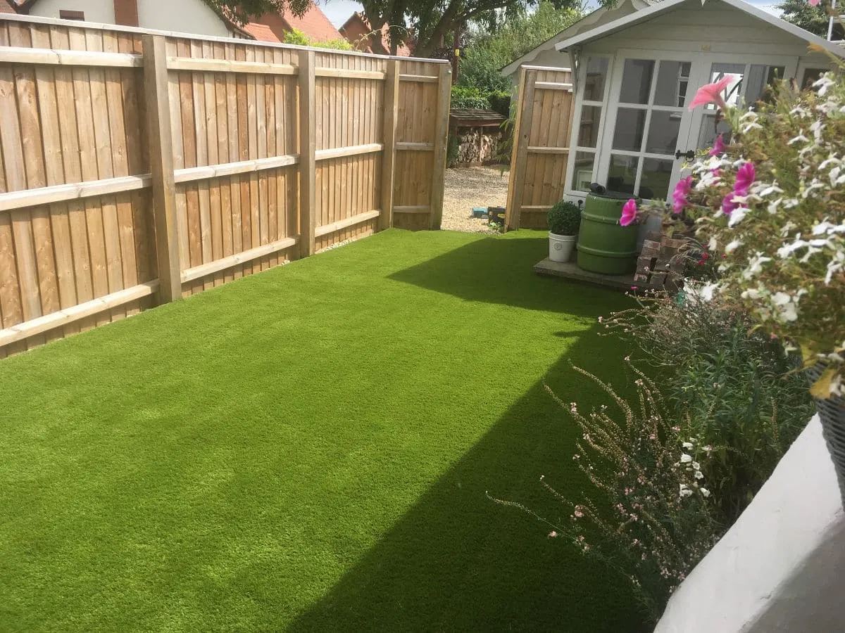 Artificial grass play area with raised sleeper beds by Stoneage Property Care