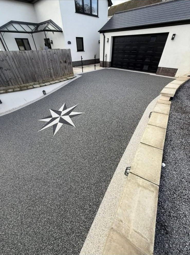 Charcoal resin driveway with a compass-rose inlay leading to a house, completed by Stoneage Property Care in Wiltshire